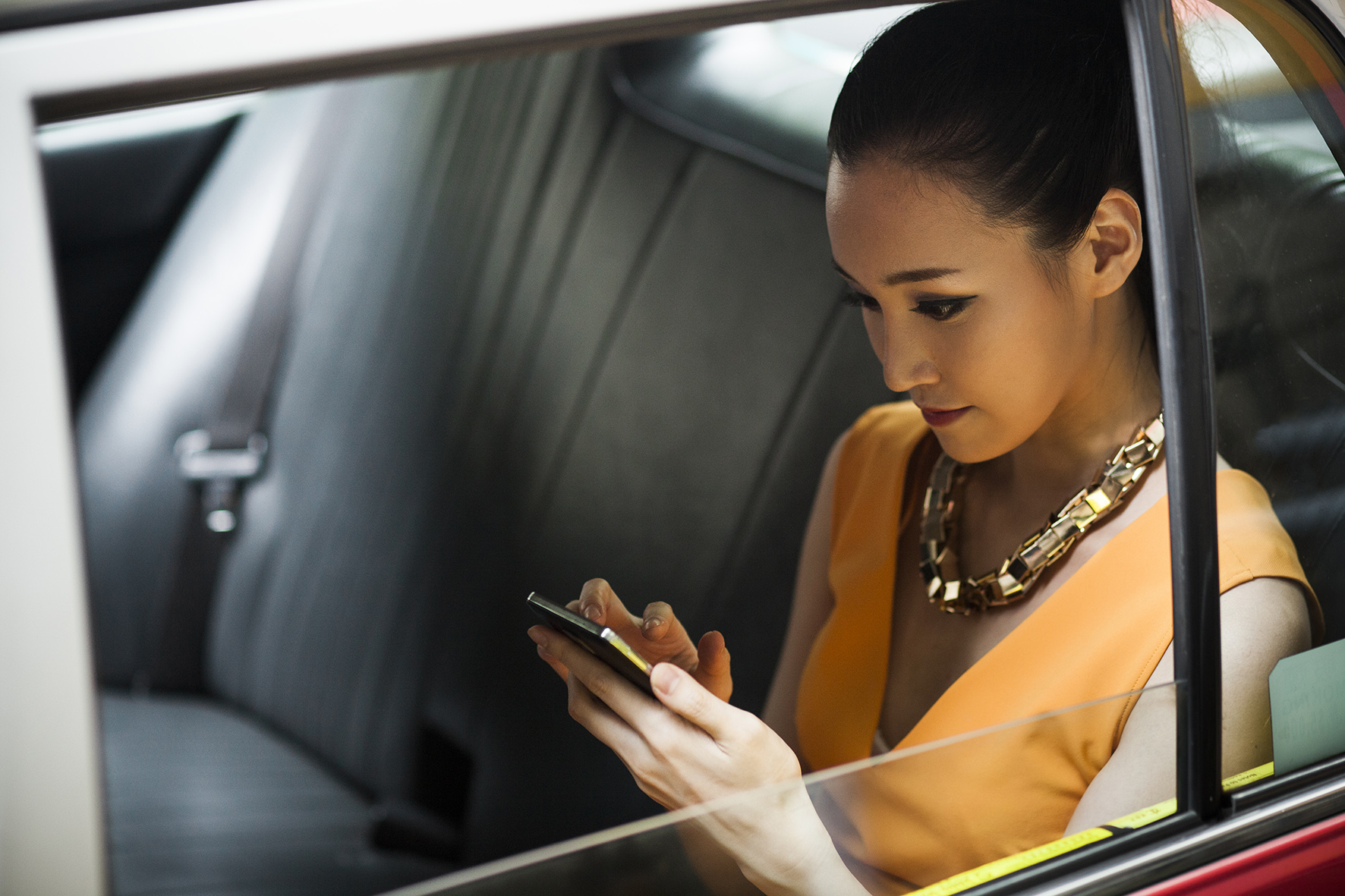 A woman is watching her phone while sitting in a car