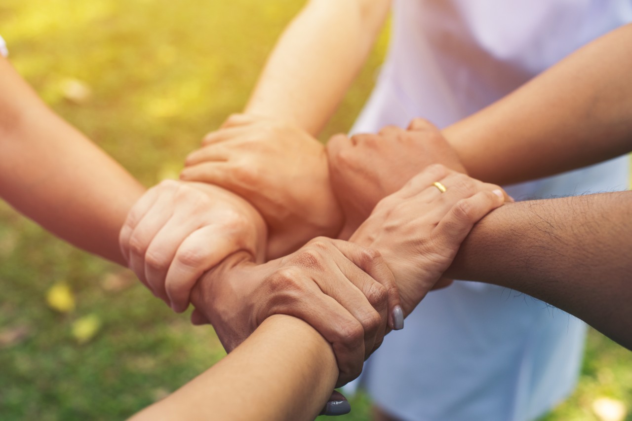 Plusieurs mains de différentes personnes se tenant ensemble, formant un cercle de solidarité et d'unité, illustrant l'importance du facteur social