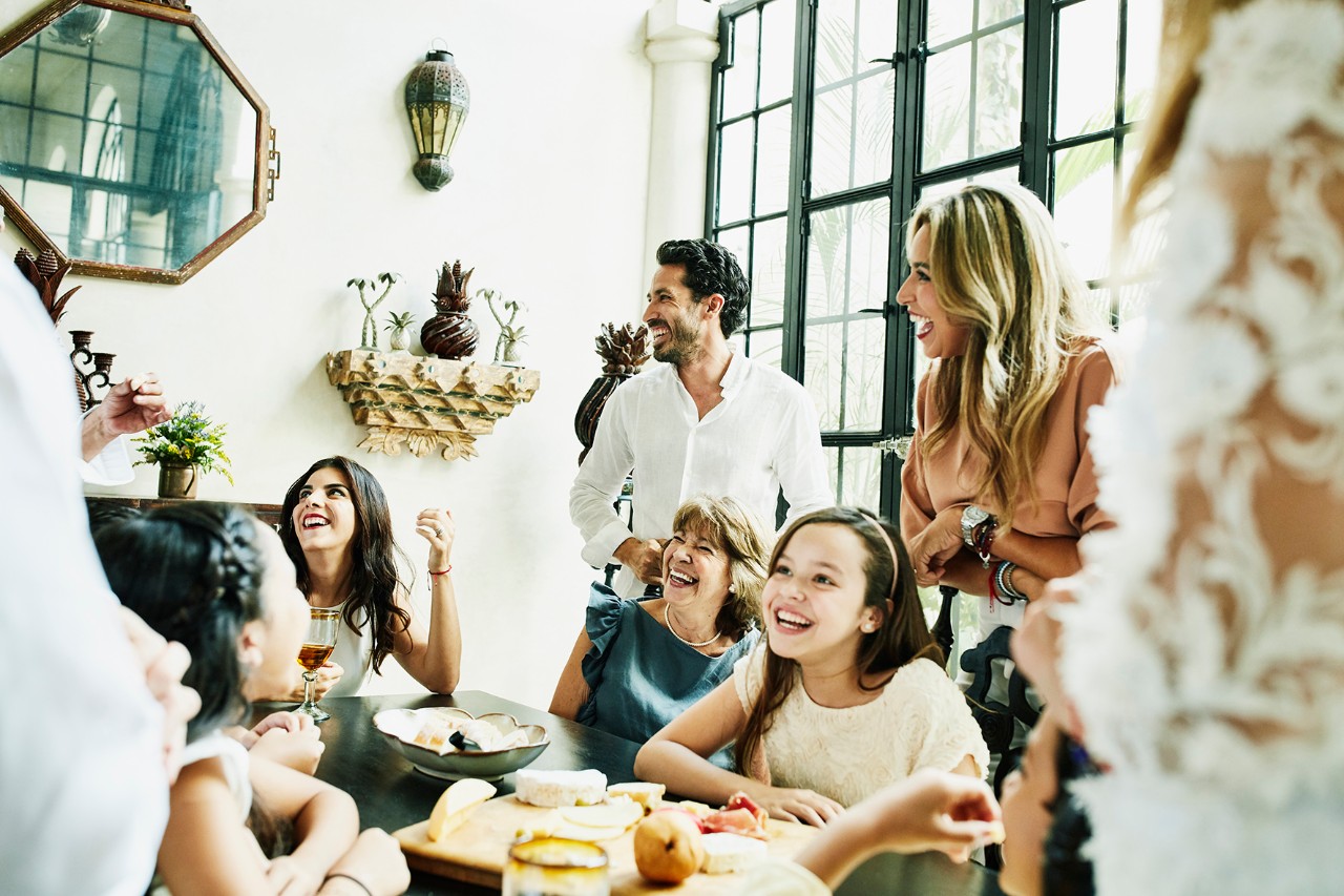 Laughing multigenerational family gathered around dining room table sharing appetizers before birthday dinner